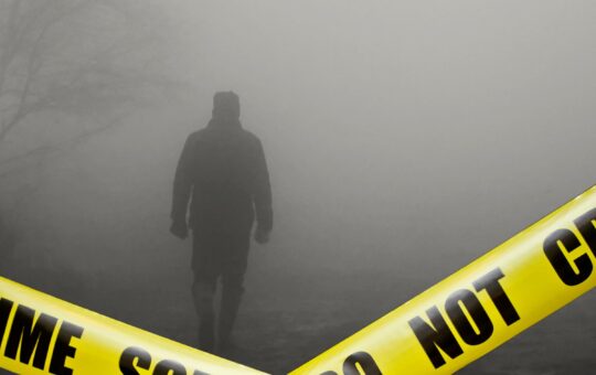 A spooky photo of a man in dark clothing walking through the fog, with 'crime scene do not enter' tape in the foreground. The scene depicts a murder scene.